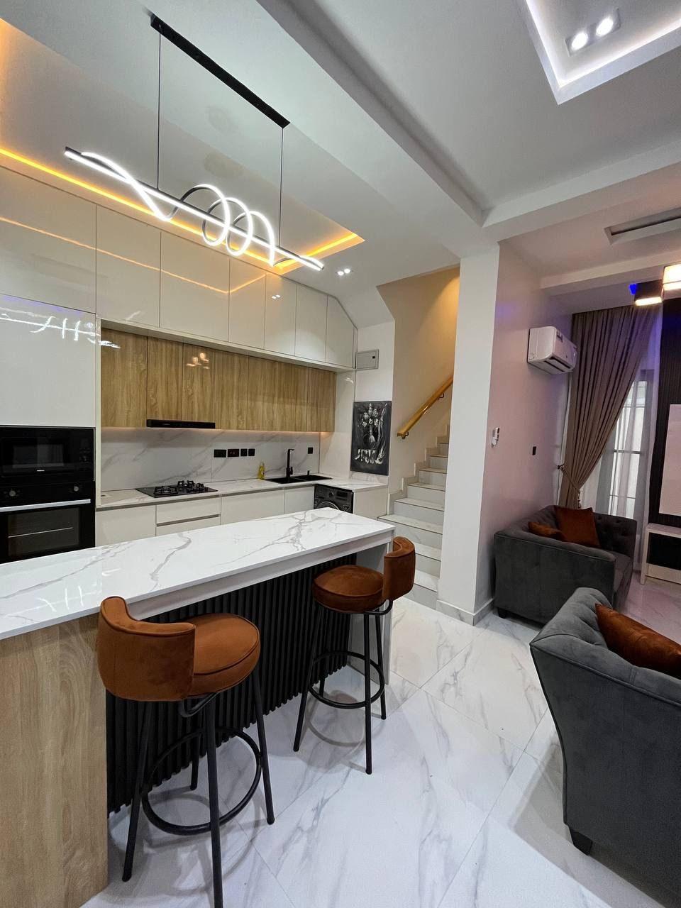 Open kitchen and lounge with a marble island, fluted base, rust stools and spiral pendant light
