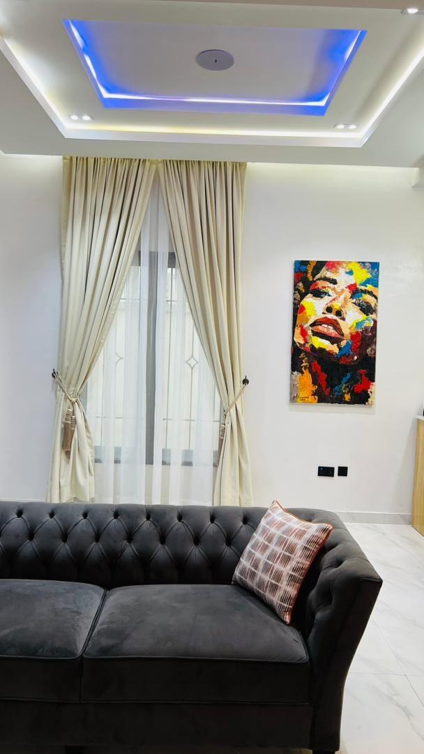 Charcoal tufted sofa beneath a colourful portrait artwork and floor-length cream curtains