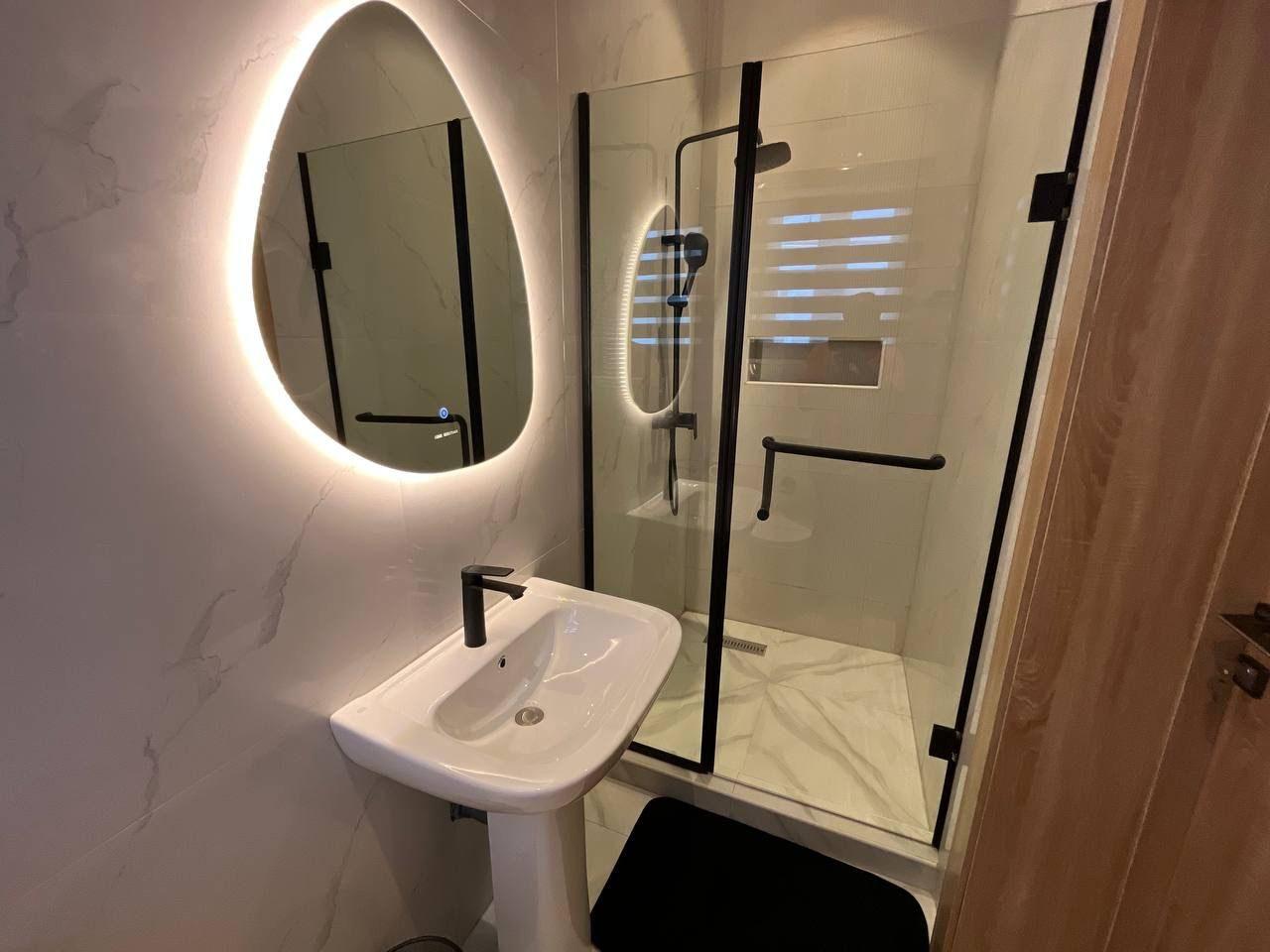 Bathroom with organic backlit mirror, pedestal basin and black-framed frameless shower screen