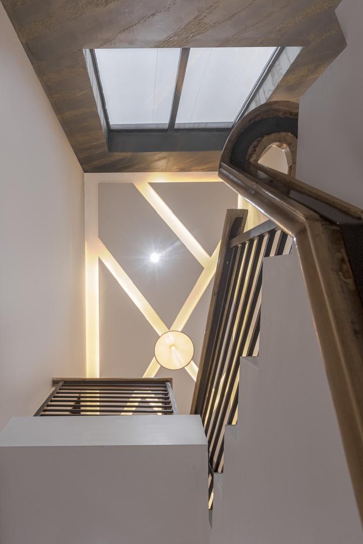 Skylit staircase with a sculpted timber handrail, slatted balustrade and geometric wall lighting