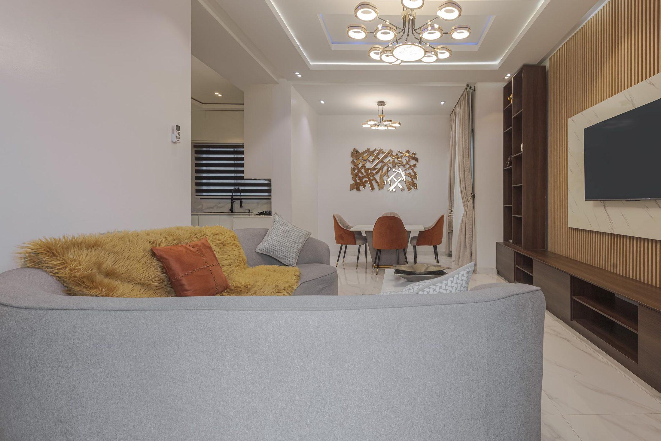 Open-plan living room by Valdo Interiors with a curved sofa, timber-slatted media wall and a dining area beyond