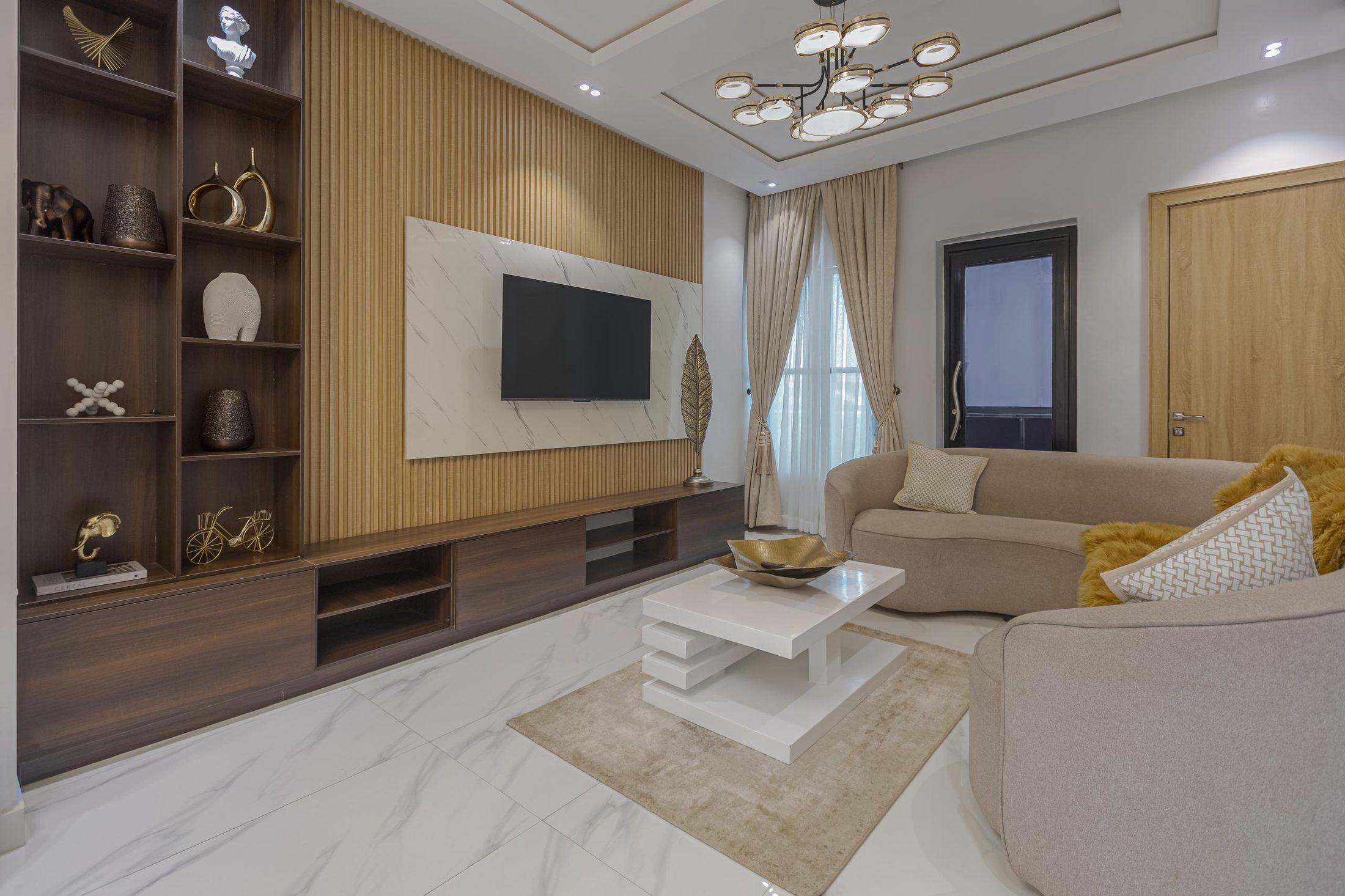 Living room with a fitted walnut shelving and media wall, marble-effect TV panel and curved neutral sofa