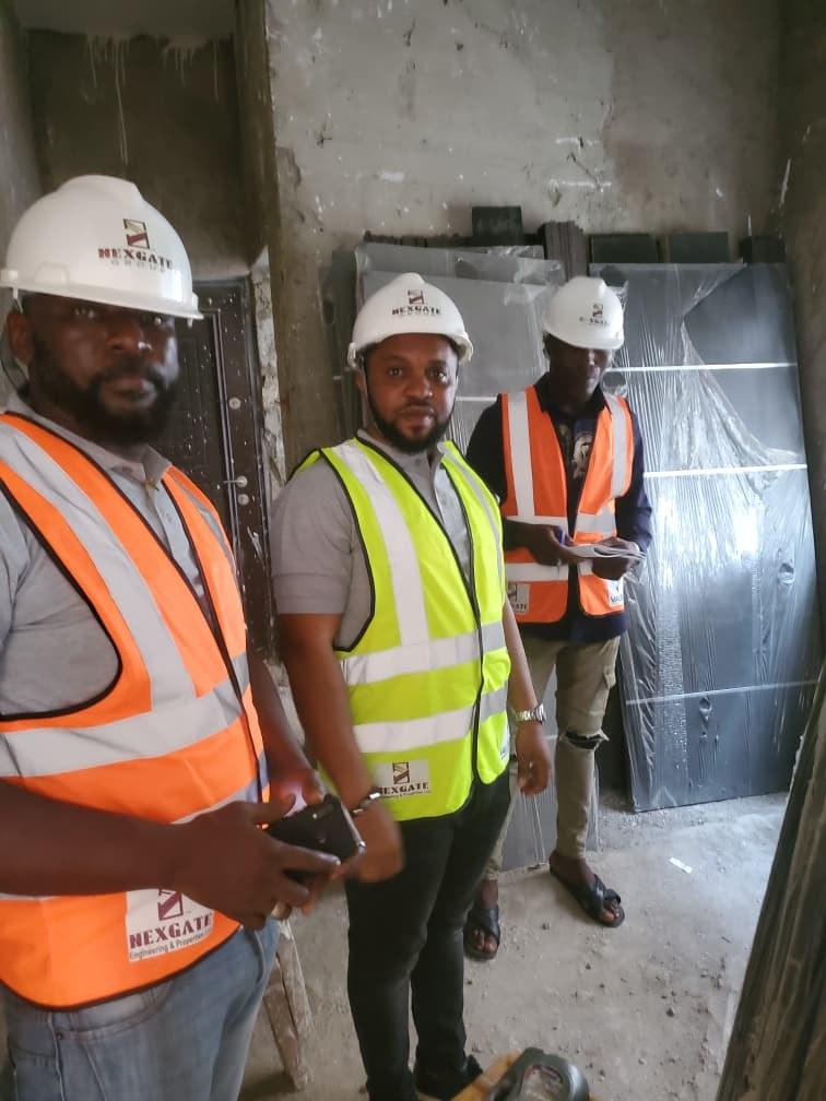 Three Nexgate team members in white hard hats and hi-vis vests in an unfinished room, with new doors in protective wrap stacked behind them