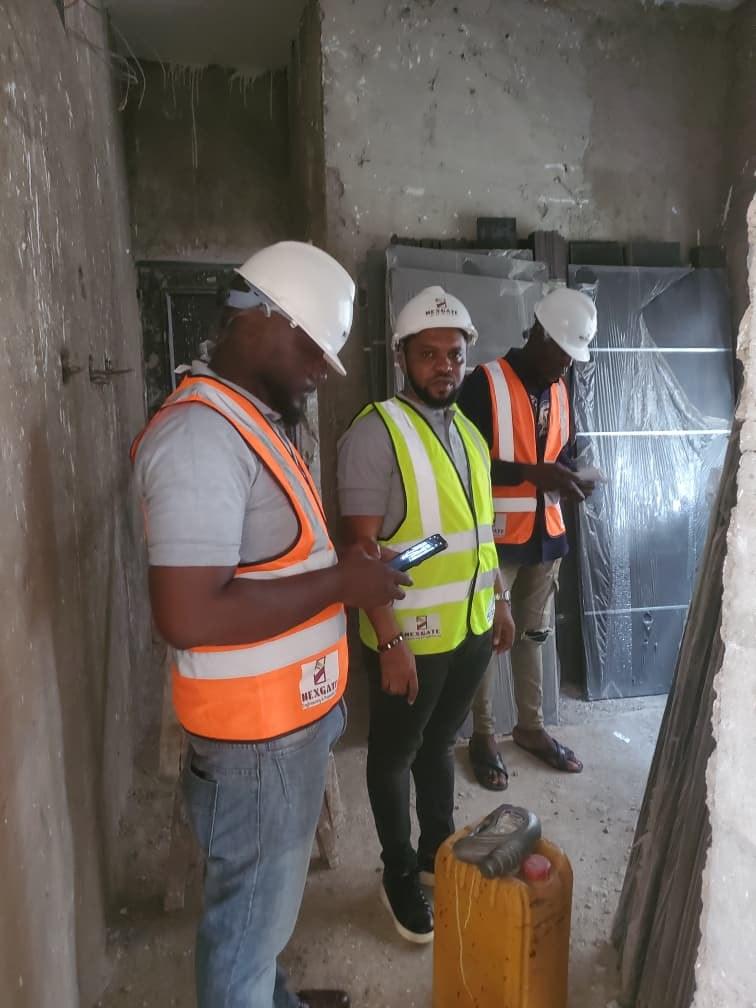 A Nexgate team member checks his phone while two colleagues in hard hats look on beside wrapped doors waiting to be fitted